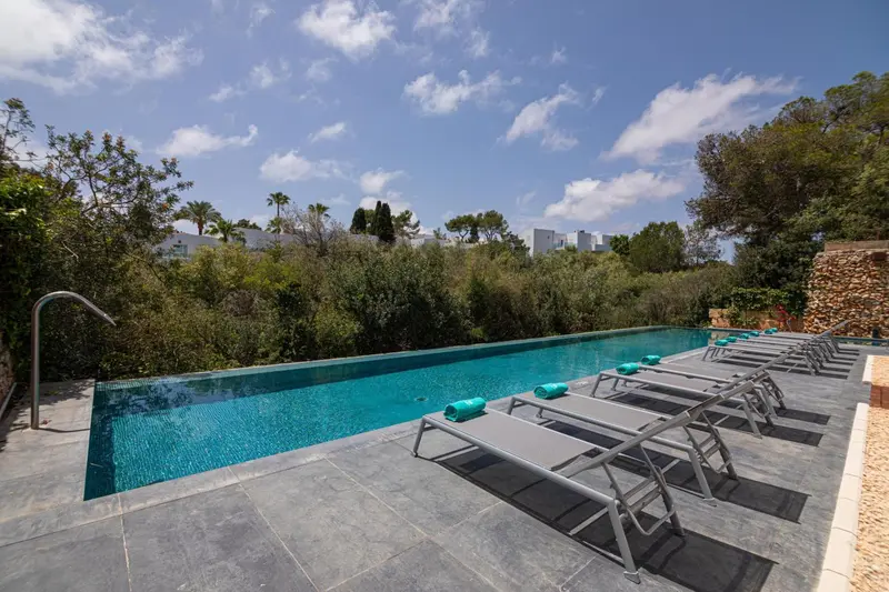 Transats gris alignés au bord d'une piscine rectangulaire bleu clair.