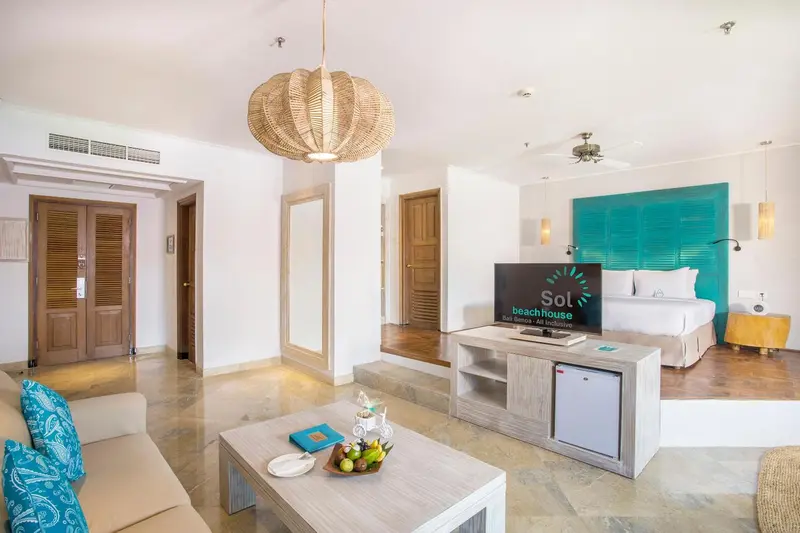 Espace de vie lumineux avec canapé, table basse et télévision face au lit.