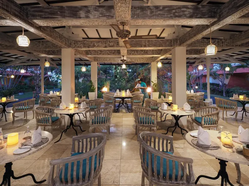 Une salle à manger extérieure avec des tables dressées et des luminaires suspendus.