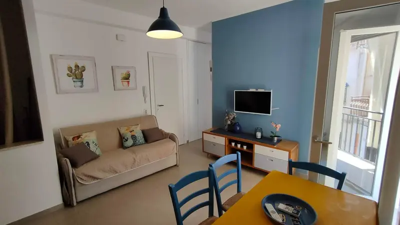 Un salon lumineux avec canapé, meuble TV et table à manger près d'une porte-fenêtre.