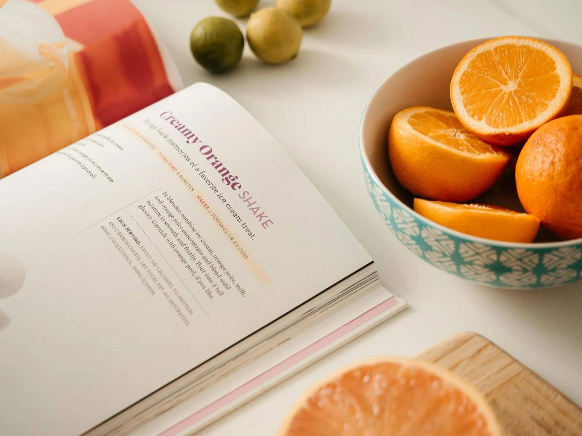 Un livre de recettes ouvert présente une recette de smoothie à l'orange, accompagné de fruits frais.