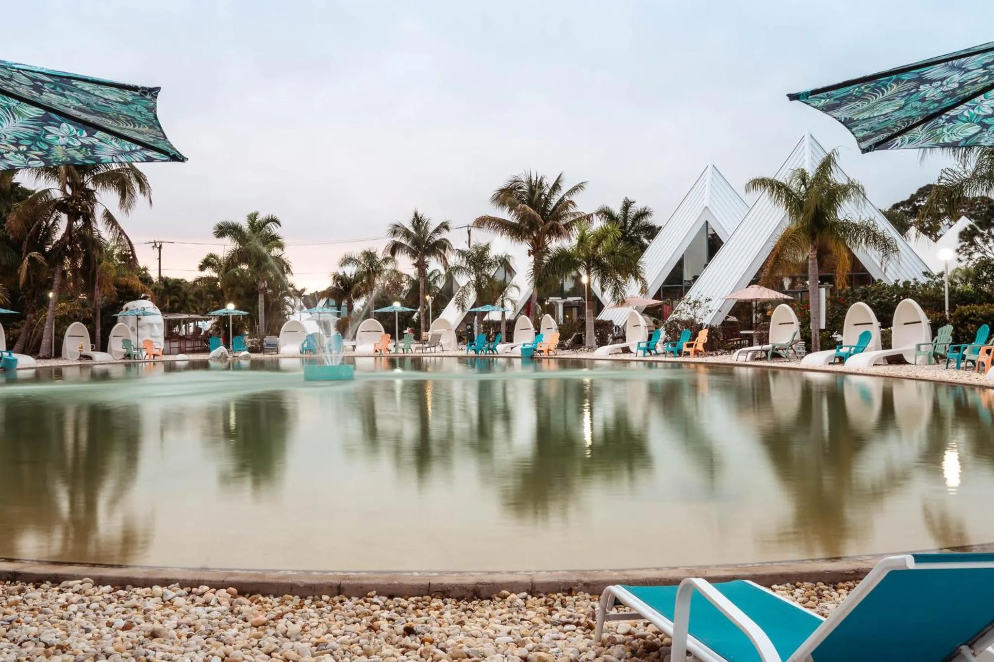 Transats bleus alignés au bord d'une piscine rectangulaire entourée de végétation tropicale.