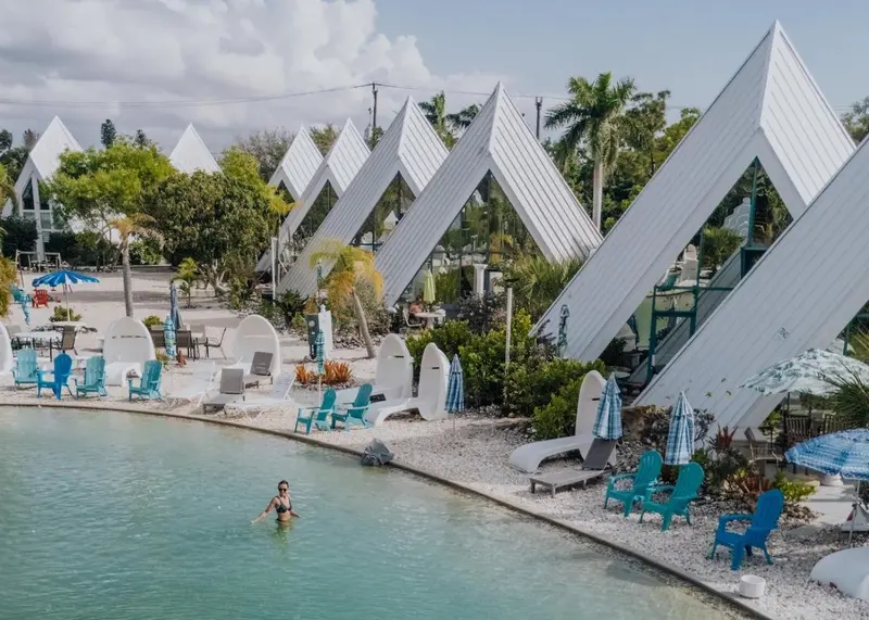 Bâtiments blancs aux toits pointus surplombent une piscine turquoise et une plage.