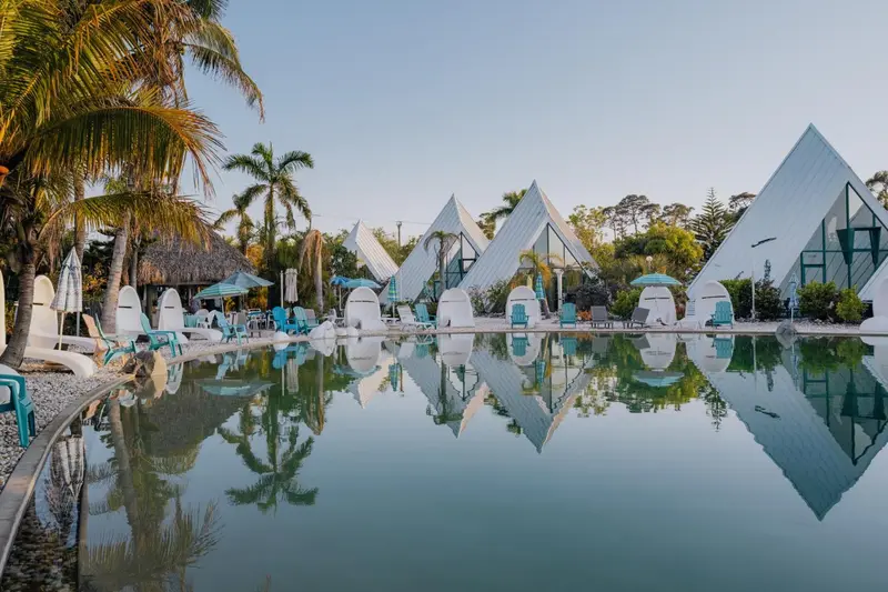 Vue d'une piscine turquoise bordée de chaises longues et de bâtiments aux toits coniques.