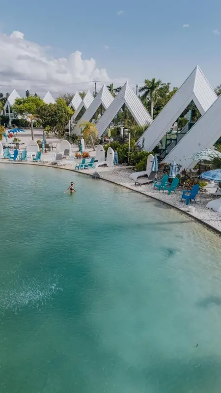 Vue aérienne d'une piscine turquoise bordée de chaises longues et de parasols.