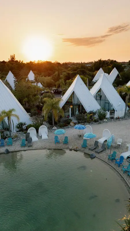 Vue aérienne d'un ensemble de bungalows blancs au bord d'une piscine turquoise.