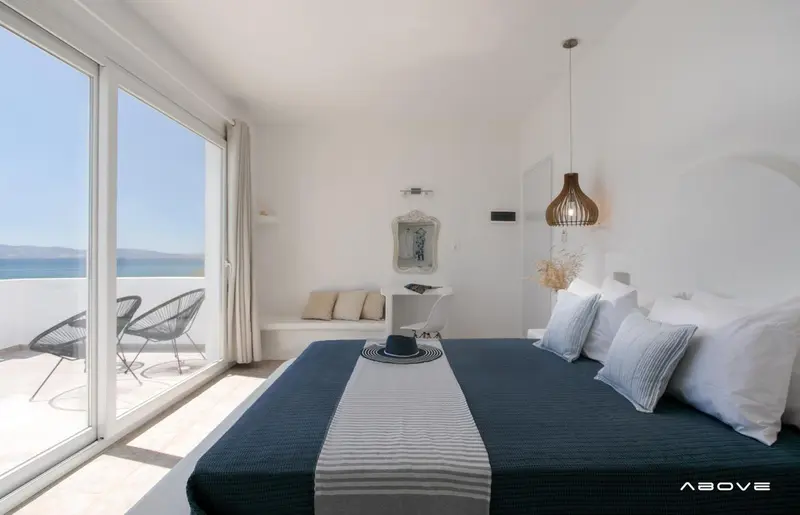 Une chambre lumineuse avec un grand lit donnant sur une terrasse et la mer.