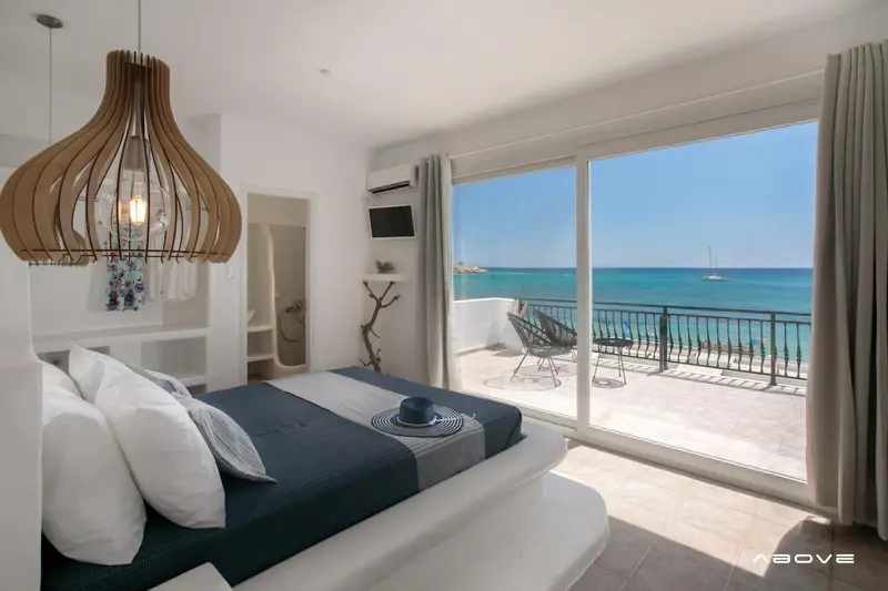 Une chambre lumineuse avec un grand lit donnant sur une vue mer et un balcon.