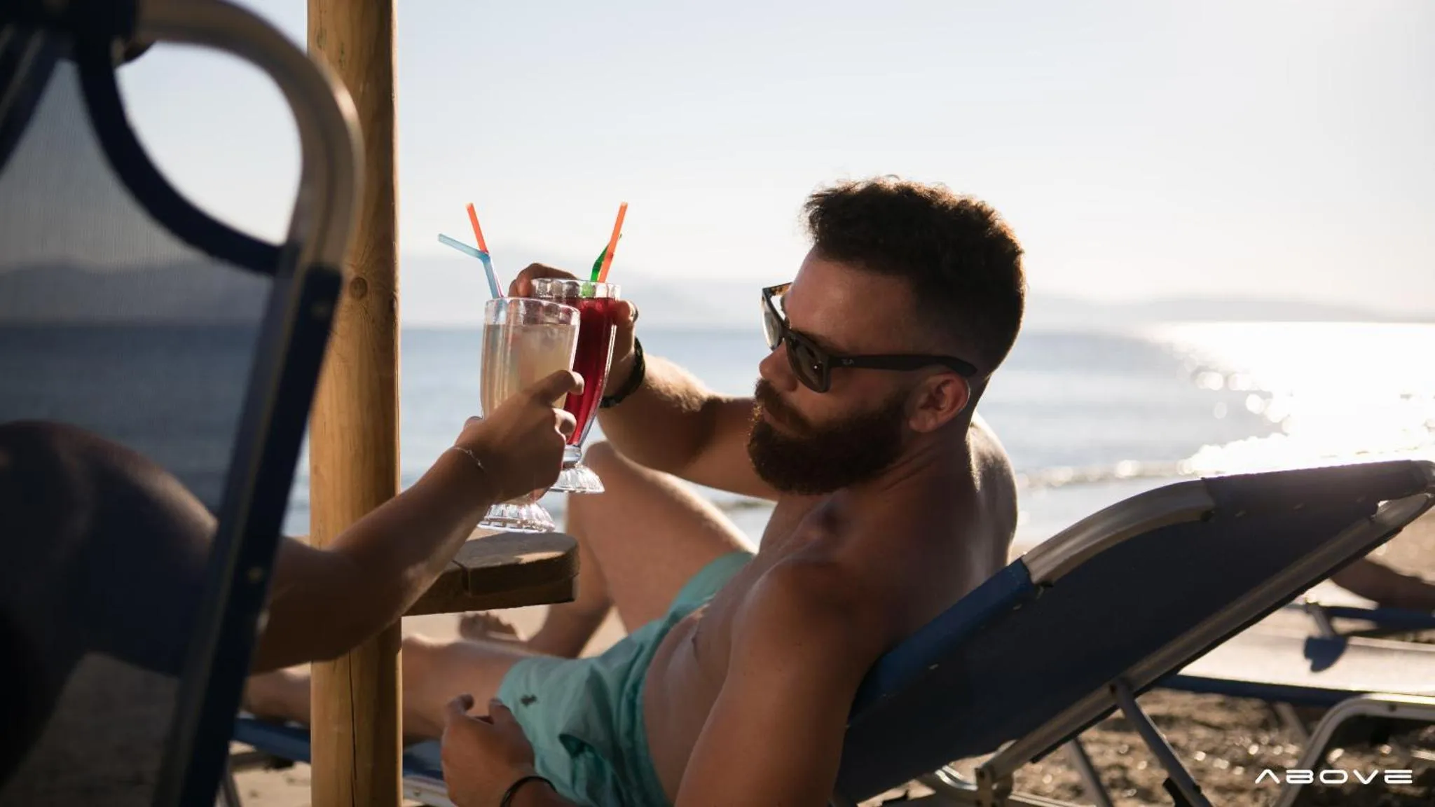 Un homme se détend sur une chaise longue avec un cocktail face à la mer.