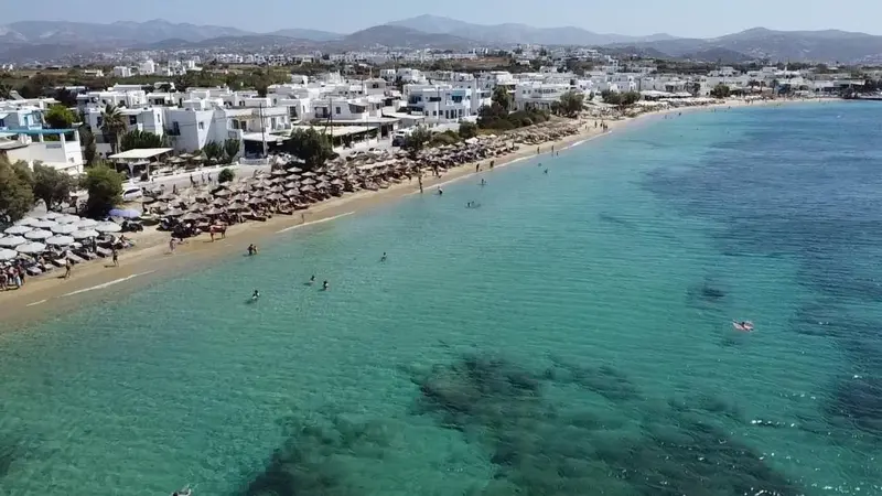 Vue aérienne d'une plage ensoleillée avec des transats et des baigneurs dans une eau turquoise.