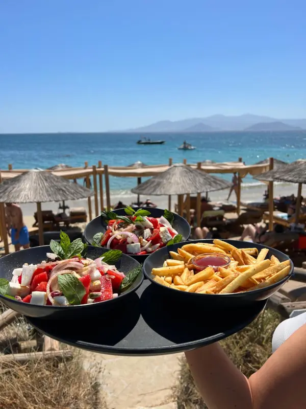 Assiettes de salade et de frites servies sur un plateau au bord de la mer.