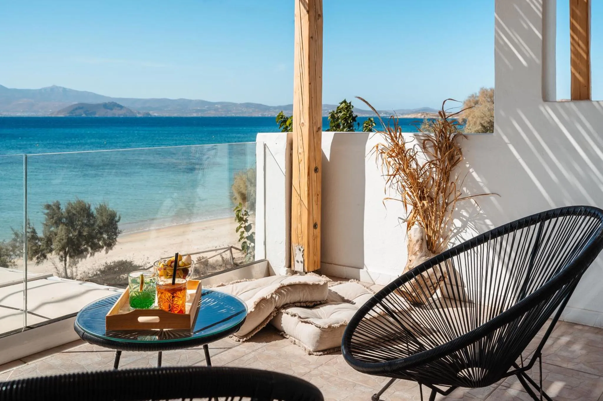 Une terrasse avec une table basse et des boissons colorées offre une vue sur la mer et la plage.