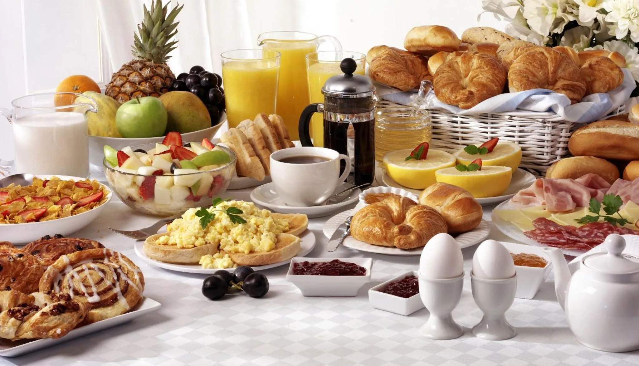 Une table garnie de viennoiseries, de fruits frais, de jus et de plats chauds.