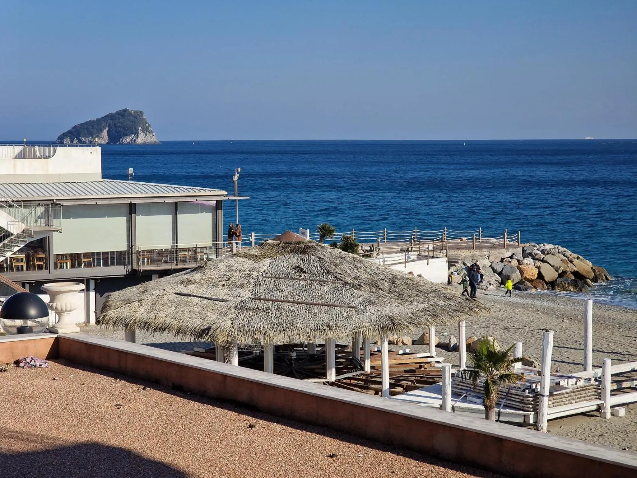 Vue sur la mer depuis une terrasse avec parasols et végétation.