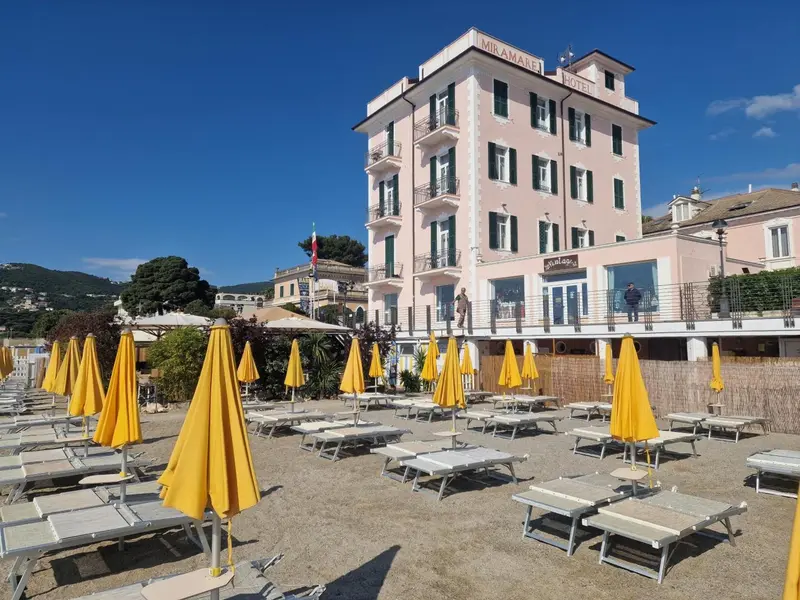 Façade d'un bâtiment rose avec des transats et parasols jaunes sur une plage.