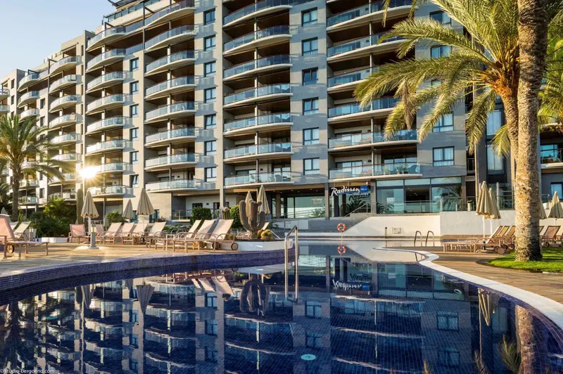 Vue d'un bâtiment moderne avec des balcons et une piscine au premier plan.