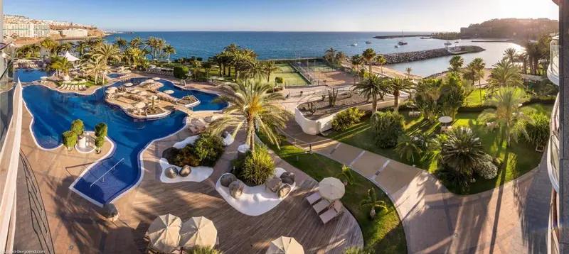 Vue aérienne sur un complexe hôtelier avec piscines et végétation luxuriante face à la mer.