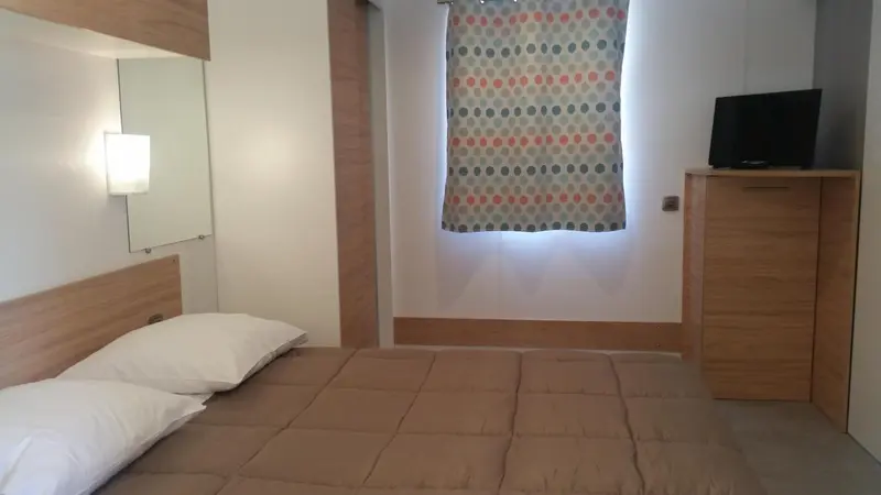 Une chambre lumineuse avec un lit double et un meuble télévision.