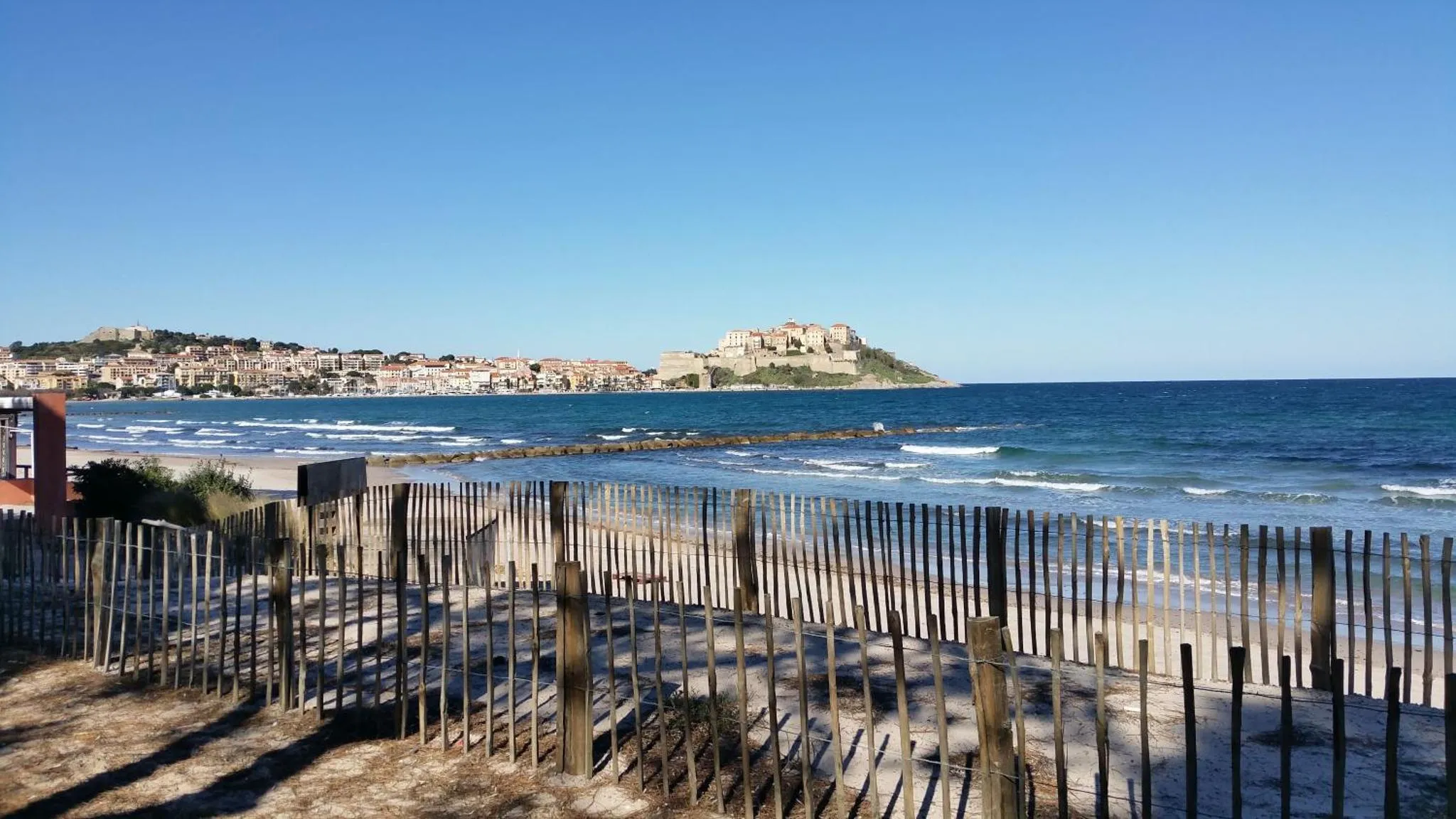 Une plage de sable avec une barrière en bois et une vue sur la mer et une ville côtière.