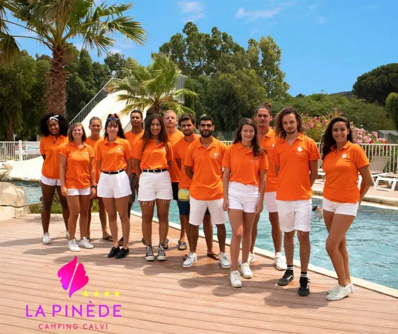 Groupe de personnes souriantes posant devant un bâtiment et une piscine.