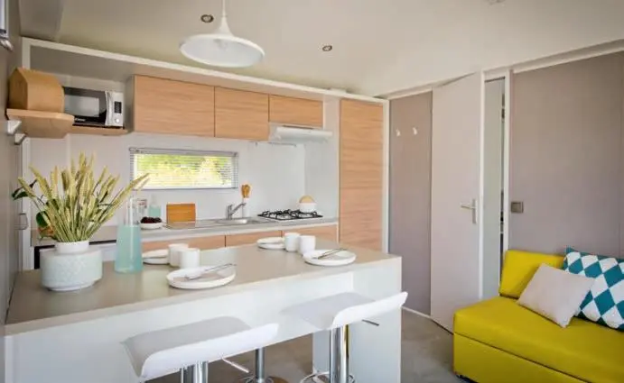 Une cuisine moderne avec un plan de travail et deux tabourets, adjacente à un coin salon jaune.