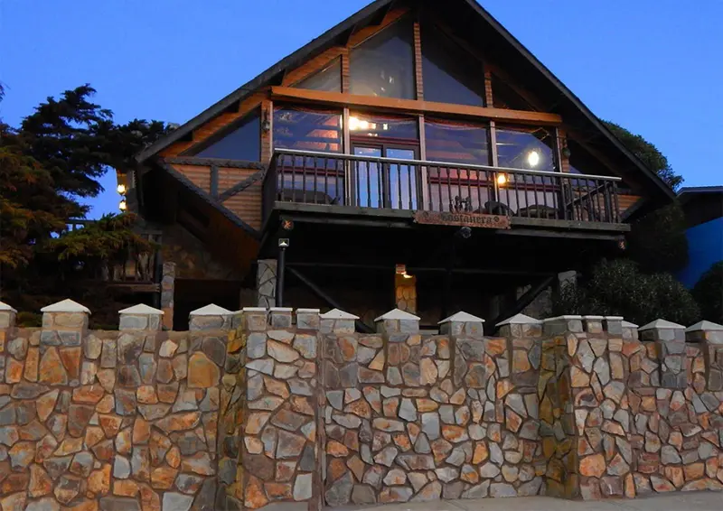 Maison en bois avec balcon et muret en pierre au crépuscule.