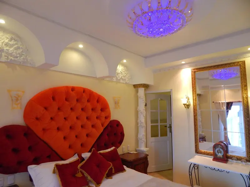 Une chambre à coucher lumineuse avec un grand lit à tête de lit capitonnée orange et un miroir doré.