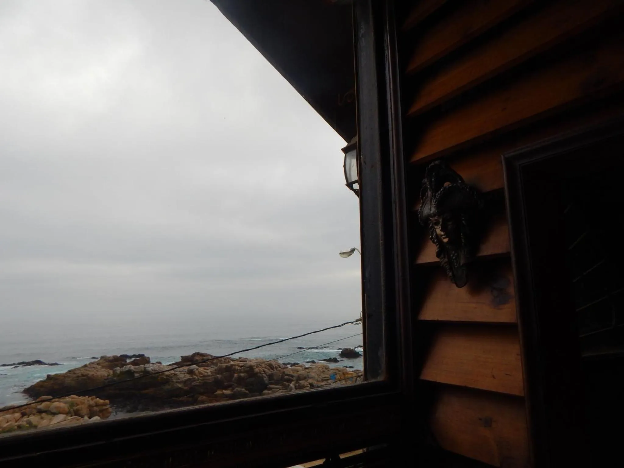 Vue sur la mer depuis une fenêtre en bois sombre.