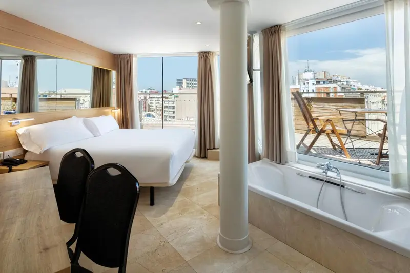 Chambre lumineuse avec un grand lit et une baignoire près de la fenêtre.