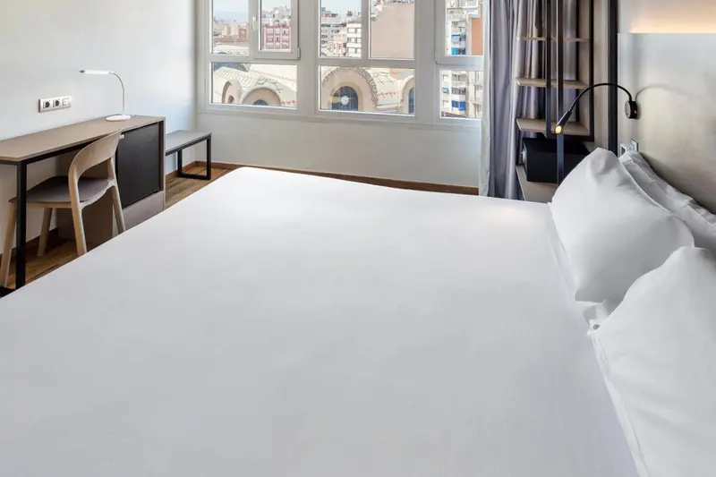 Une chambre lumineuse avec un grand lit et un bureau près de la fenêtre.