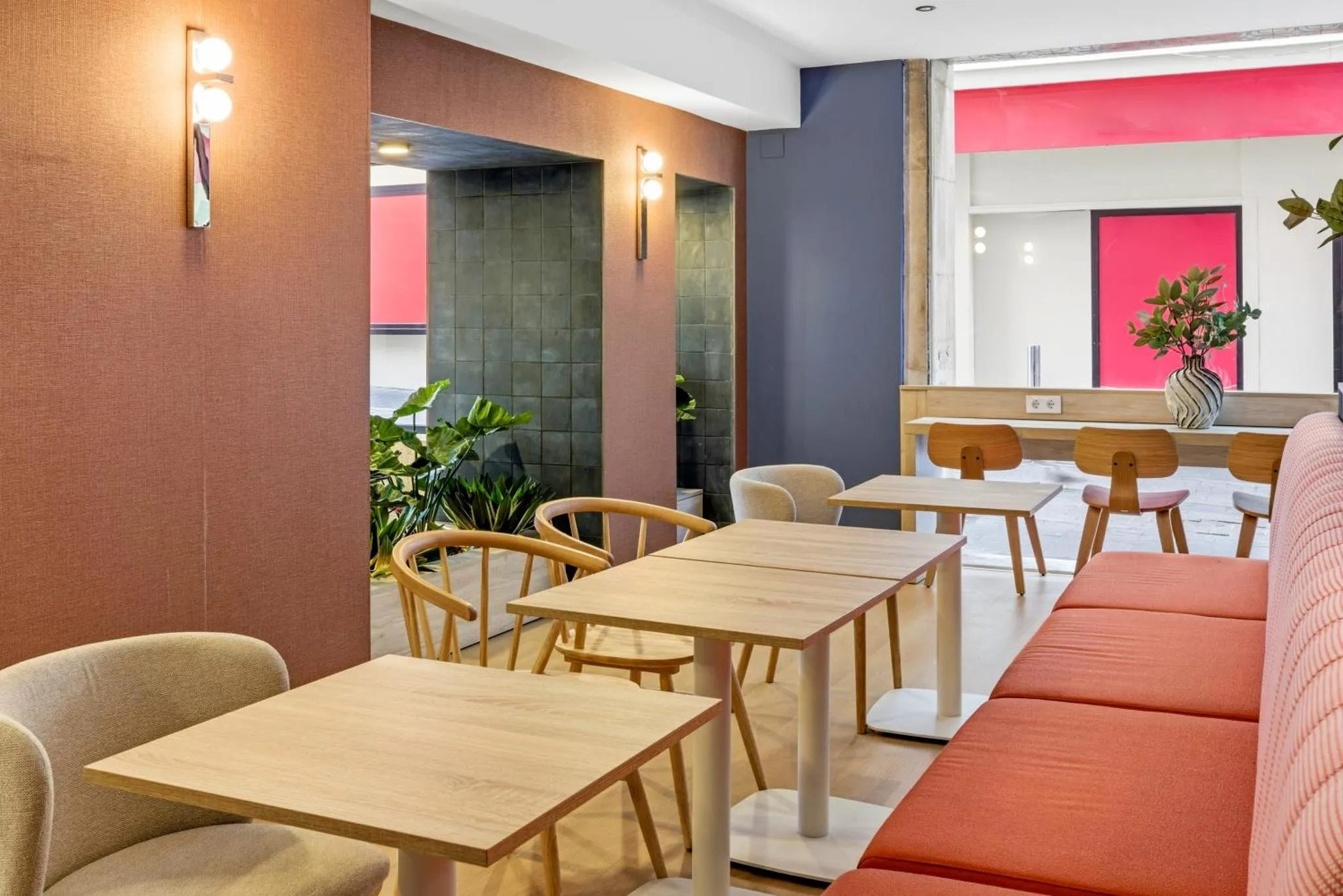 Une salle lumineuse avec des tables et des chaises en bois, ainsi qu'un canapé orange.