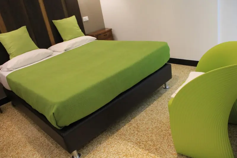 Une chambre avec un lit recouvert d'une couverture verte et deux fauteuils.