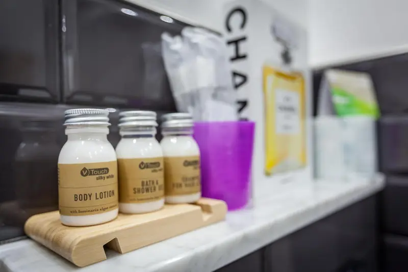 Petits flacons de produits de toilette disposés sur un plateau en bois clair dans une salle de bain.