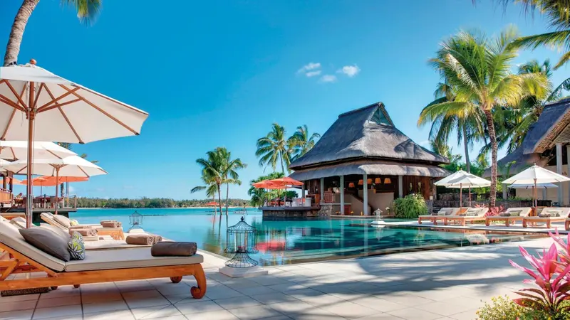 Transats blancs disposés au bord d'une piscine turquoise bordée de végétation tropicale.