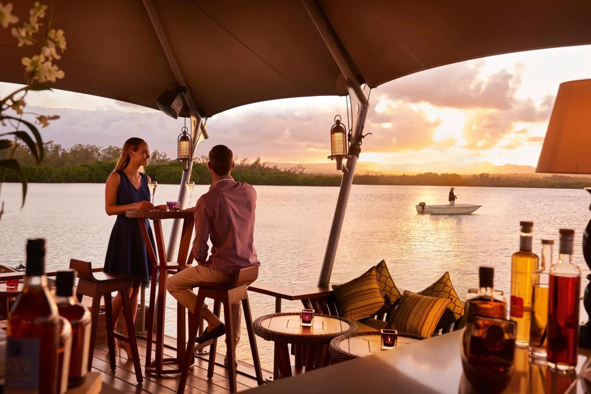 Un couple déguste des boissons sur une terrasse face à un coucher de soleil sur l'eau.