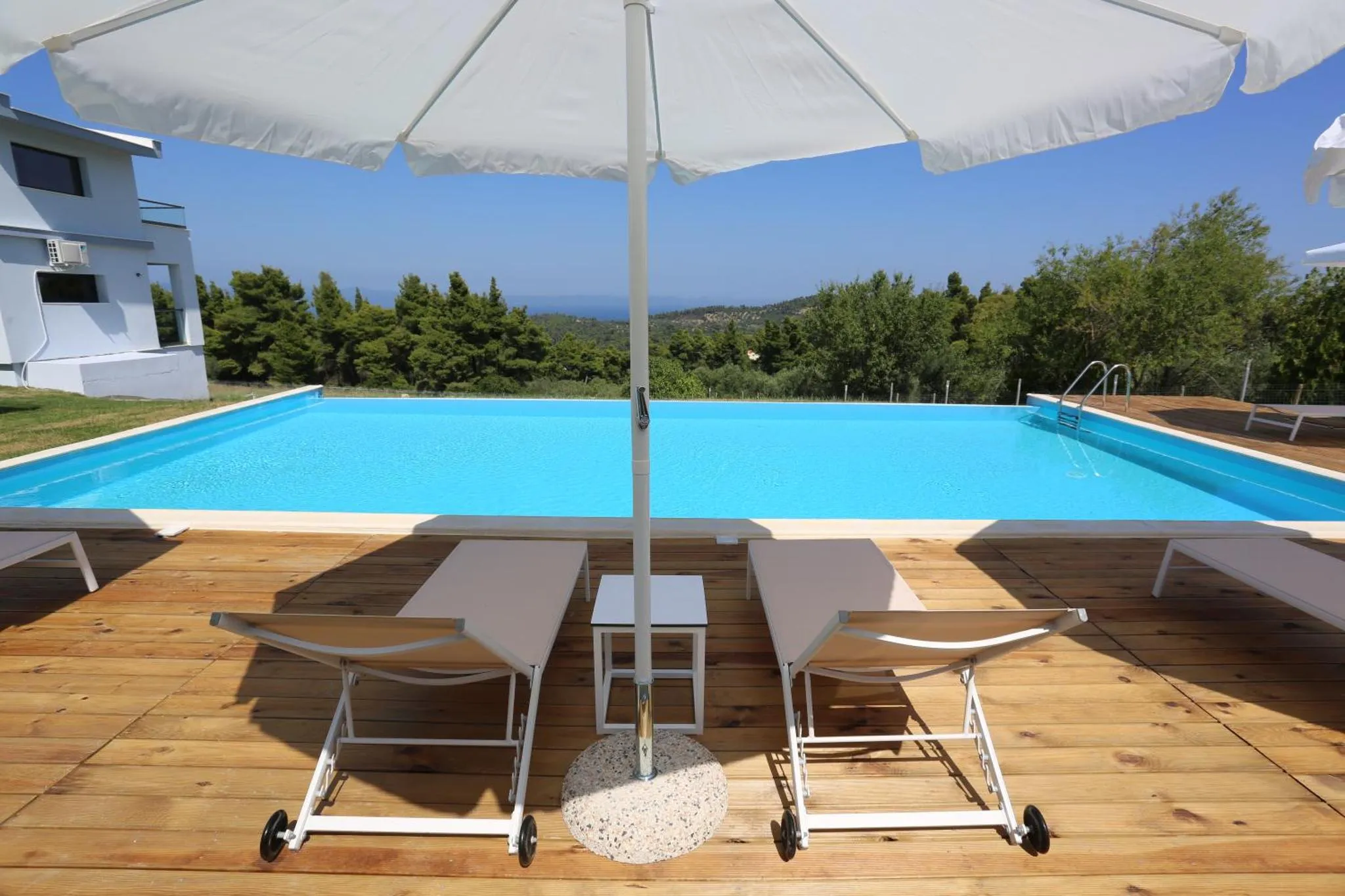 Transats blancs disposés au bord d'une piscine rectangulaire turquoise.