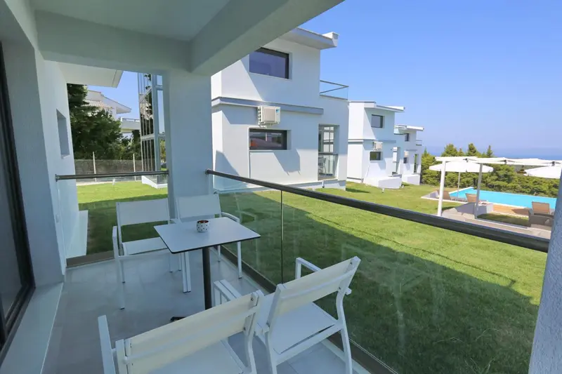 Terrasse avec mobilier blanc donnant sur une pelouse et une piscine.