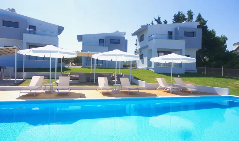 Transats blancs disposés autour d'une piscine turquoise devant des bâtiments blancs.