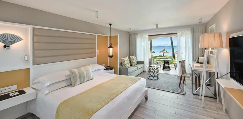 Chambre lumineuse avec un grand lit et un espace salon donnant sur une terrasse.