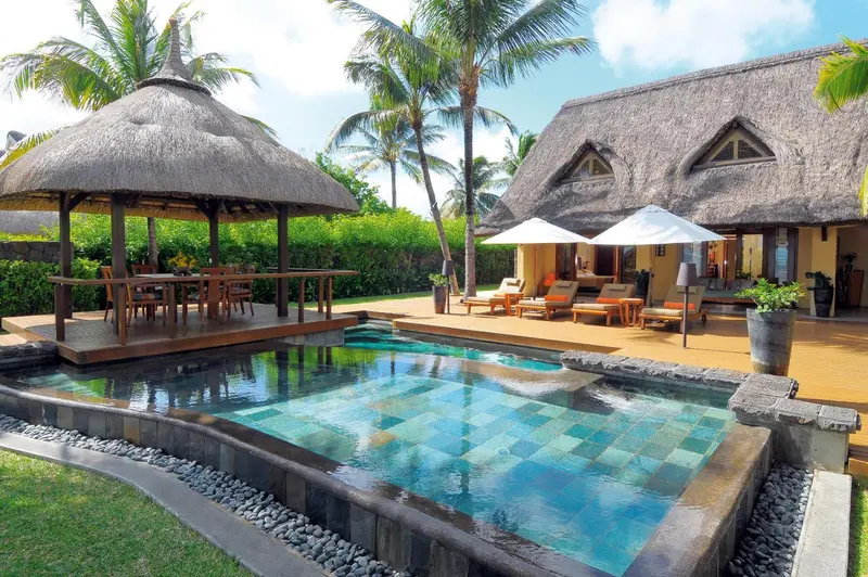 Petite piscine rectangulaire bordée d'une terrasse en bois et de végétation tropicale.