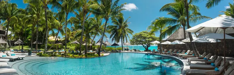 Une piscine bordée de transats et de palmiers sous un ciel bleu.