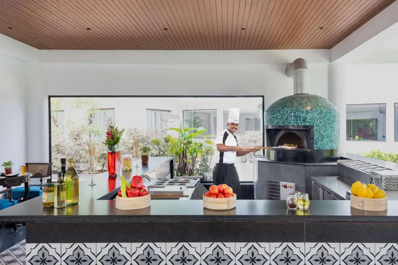 Un chef prépare une pizza dans un four à bois en extérieur.