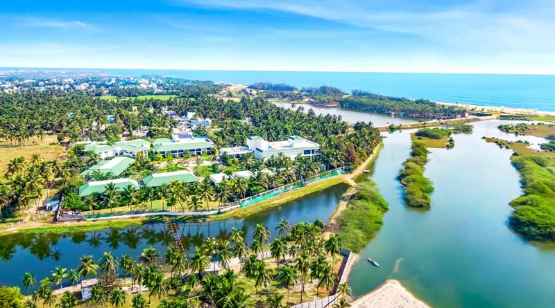 Vue aérienne d'un complexe hôtelier bordé de végétation luxuriante et d'une étendue d'eau.