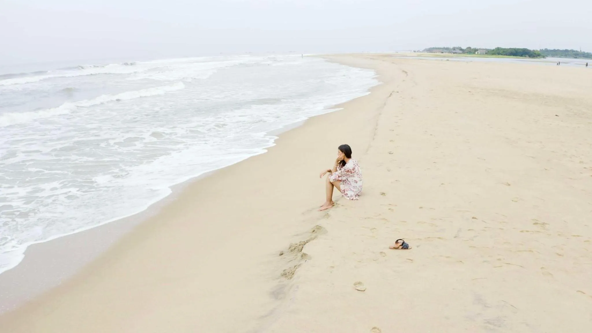Une personne assise sur une plage de sable fin, face à l'océan.