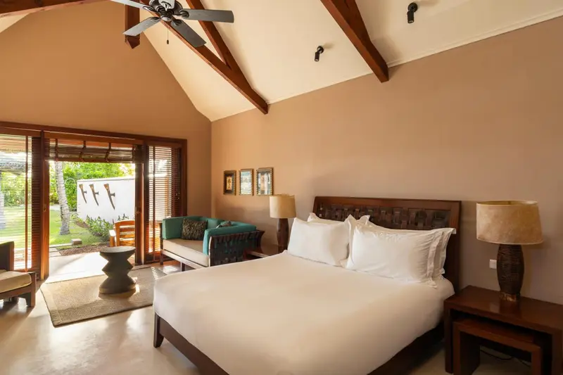 Une chambre lumineuse avec un grand lit et un coin salon donnant sur l'extérieur.