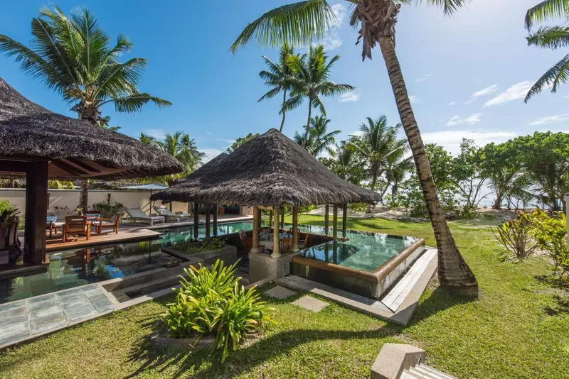 Petites piscines privées avec des parasols de chaume dans un jardin tropical.
