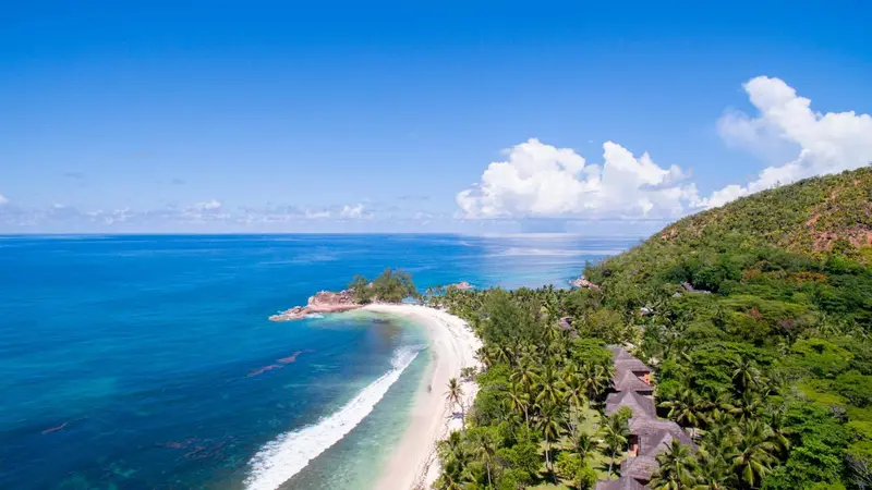 Vue aérienne d'une plage de sable blanc bordée de végétation luxuriante et d'eaux turquoise.