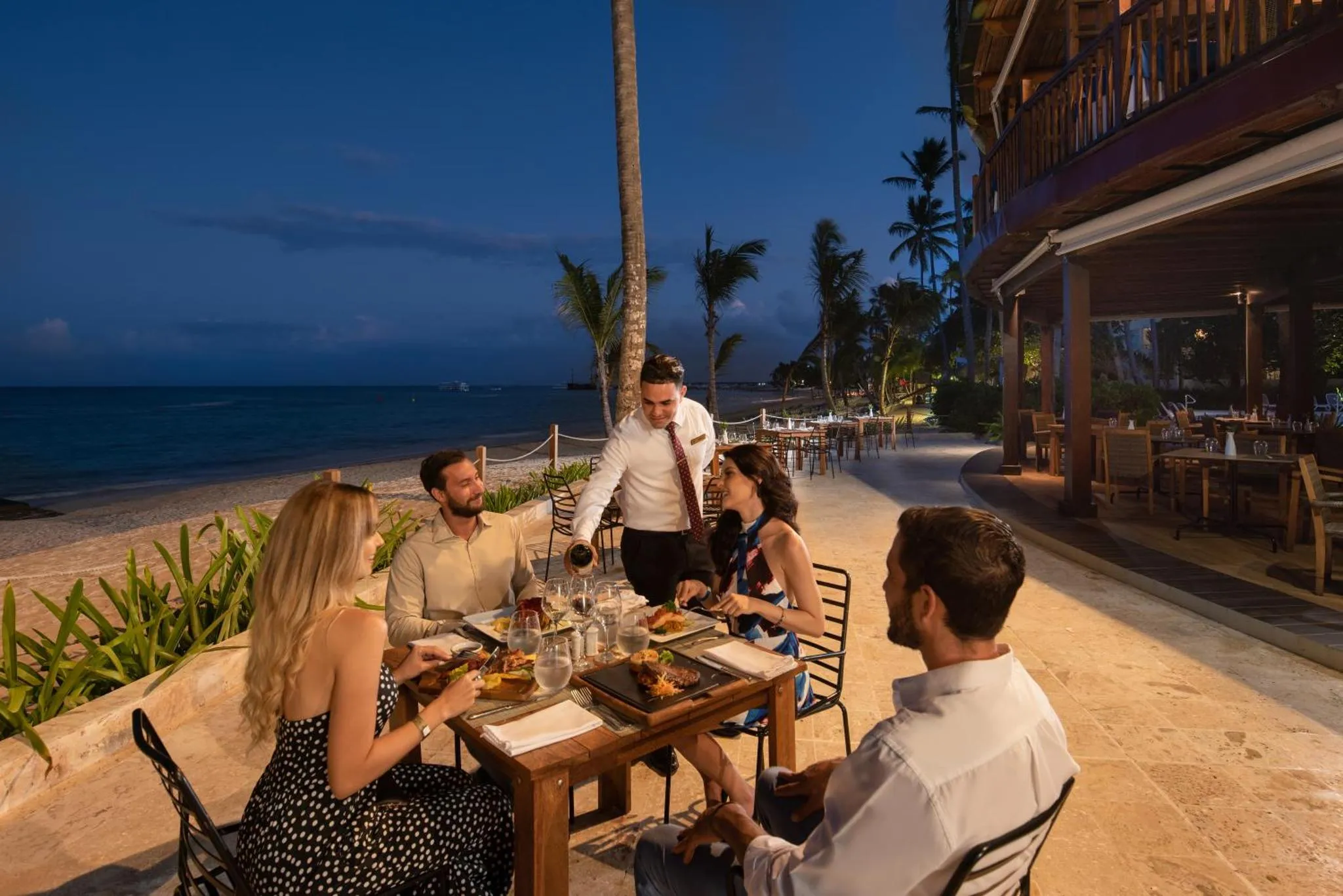 Des convives sont servis à table dans un restaurant en bord de mer au crépuscule.