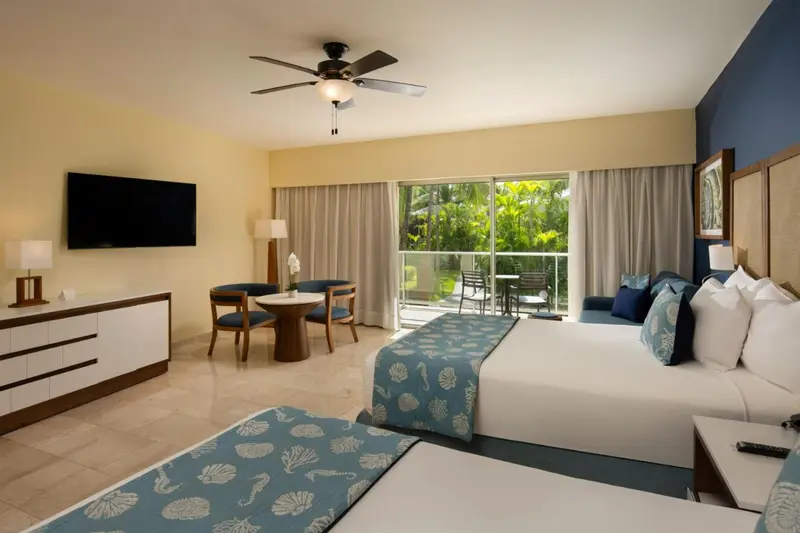 Une chambre lumineuse avec un lit double et un coin repas près d'une baie vitrée.