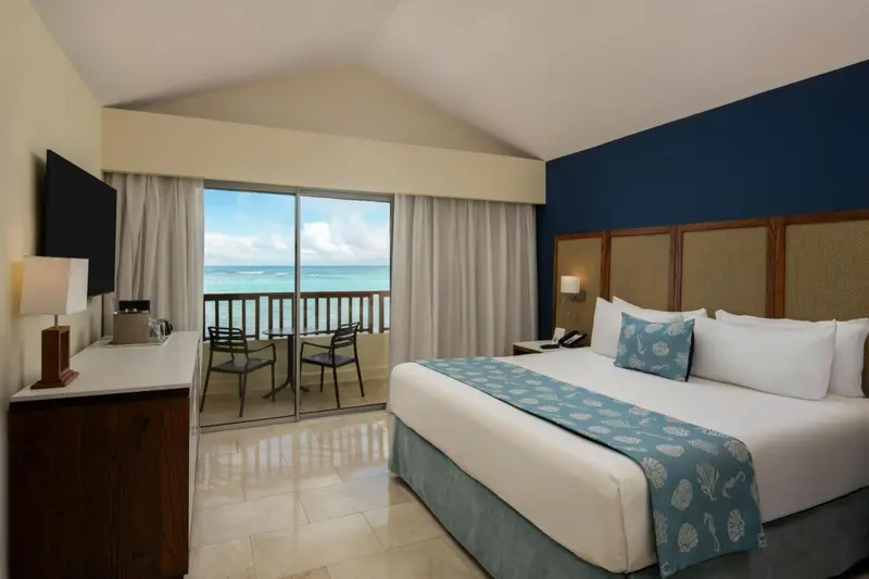 Chambre lumineuse avec un grand lit et une vue sur la mer depuis un balcon.